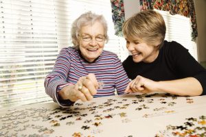 Elderly woman and a younger woman work on a jigsaw puzzle.