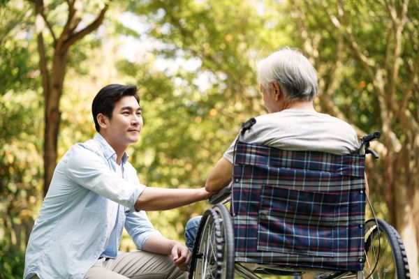 Asian son talking to and comforting wheelchair bound father